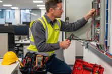 Licensed electrician performing commercial electrical installation with tools in a modern office